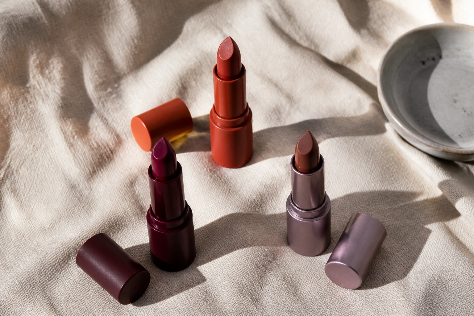 Berry, brick, and brown lipsticks uncapped on linen