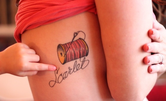 Ribcage tattoo of a wooden spool with pink thread spelling a name