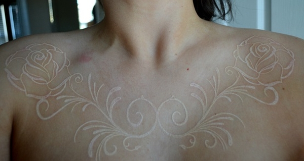 White ink rose and filigree tattoo across collarbones