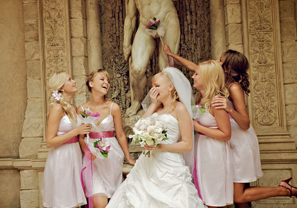 Bride and bridesmaids laughing as a bouquet covers a classical statue