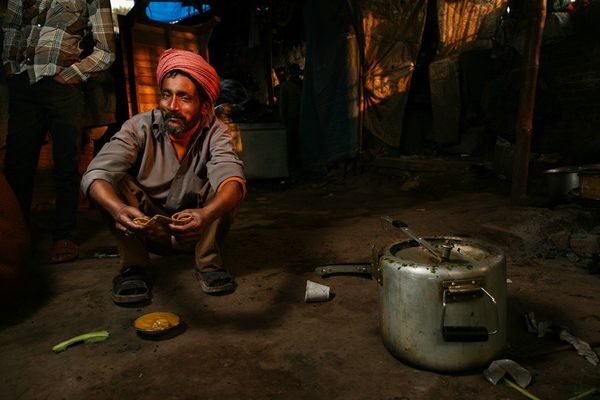 Man in orange turban eating with a pressure cooker nearby