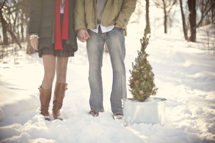 Couple holding hands in snow beside a potted evergreen