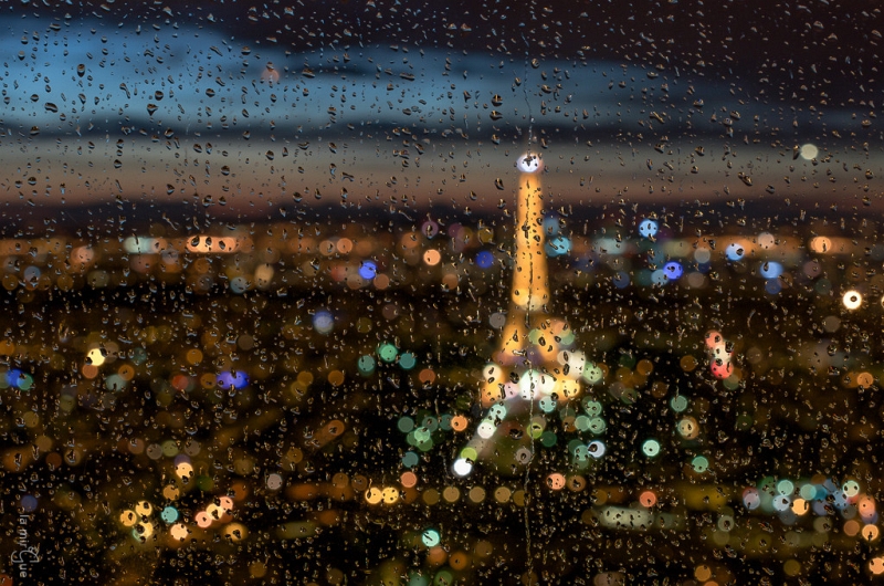 Eiffel Tower soft-focus through raindrops on glass at night