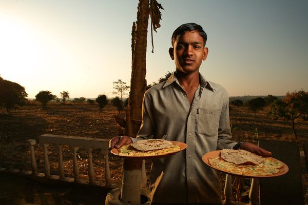 Young man holding two plates of food at sunset
