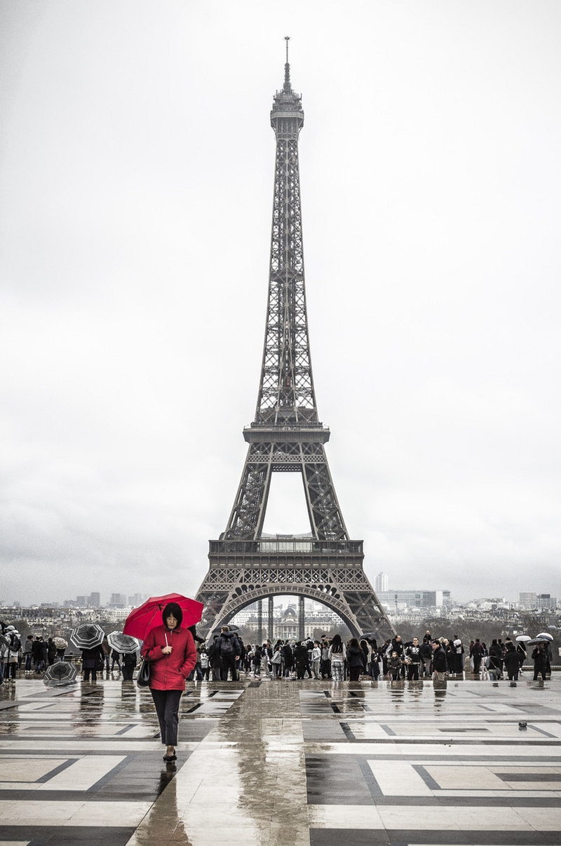 Woman in red jacket and red umbrella on wet Trocadéro paving with Eiffel Tower