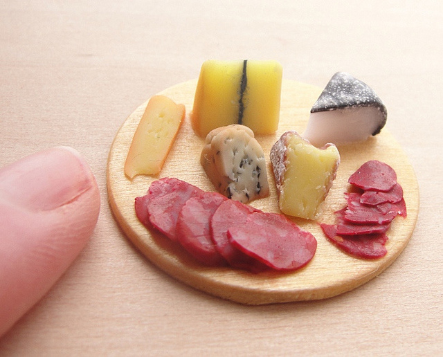 Round wooden board of miniature artisanal cheeses and cured meats