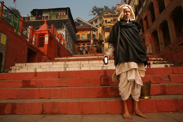 Elderly man with metal cup on red-painted ghat steps