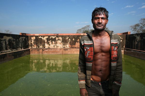 Man in open striped hoodie before a green water tank
