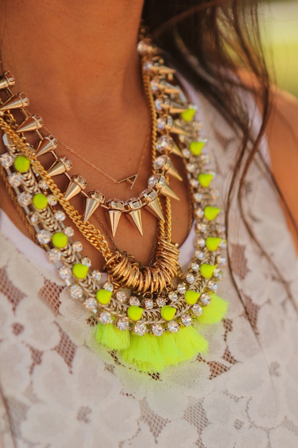 Layered gold spike and neon yellow tassel necklaces over white lace