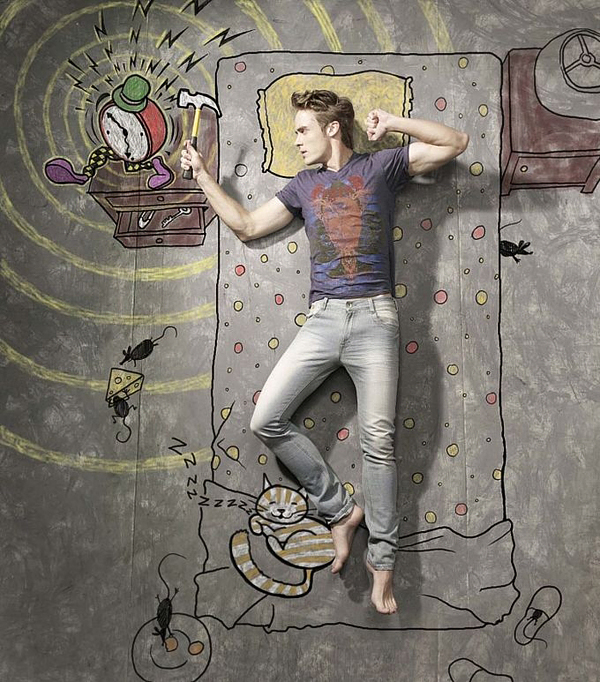 Man in bed raising a hammer at a chalk alarm clock while a cat sleeps