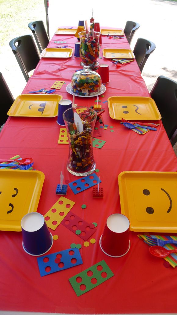 Red LEGO party table with yellow face plates and brick-filled centerpieces
