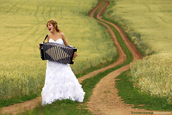 Bride playing accordion and singing on a rural dirt road