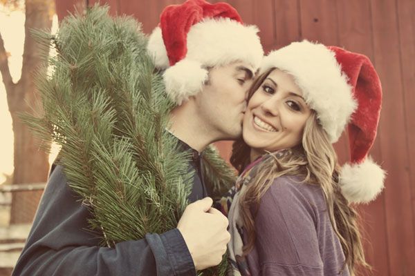 Couple in Santa hats with evergreen branches by a red barn
