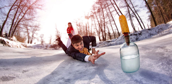 Groom crawling across ice toward a bottle while the bride holds his leg