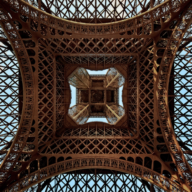 Looking straight up through concentric iron arches of the Eiffel Tower by day