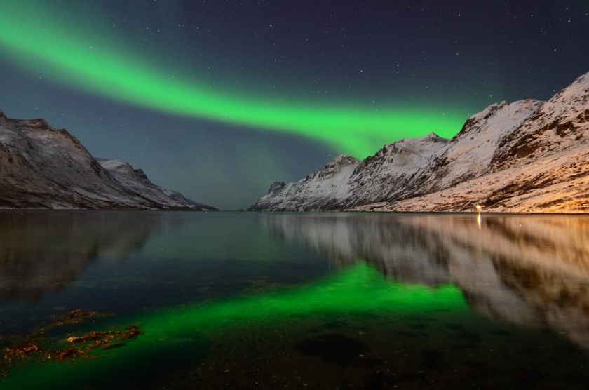 Green aurora reflected in still water between snowy mountains